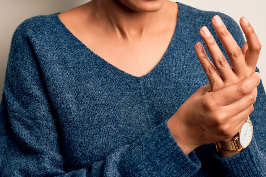 Arthritis-Doctor Close up of a woman in a blue sweater massaging one aching hand with the other. Get help for arthritis from Julie Kane, NP of Trua Health & Wellness in Alaska.
