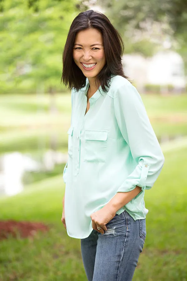 Perimenopause-Treatment A middle-aged brunette woman in a light green button-up shirt stands outside smiling, happy with her perimenopause treatment from Julie Kane, NP of Trua Health & Wellness in Alaska.